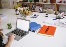 Woman works on a laptop in a stylish office, surrounded by books and documents.